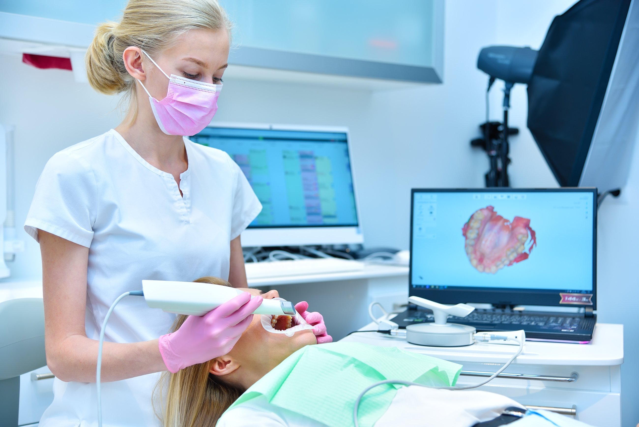 Dentist scaning patient with dental intraoral scanner and controls process on laptop screen.